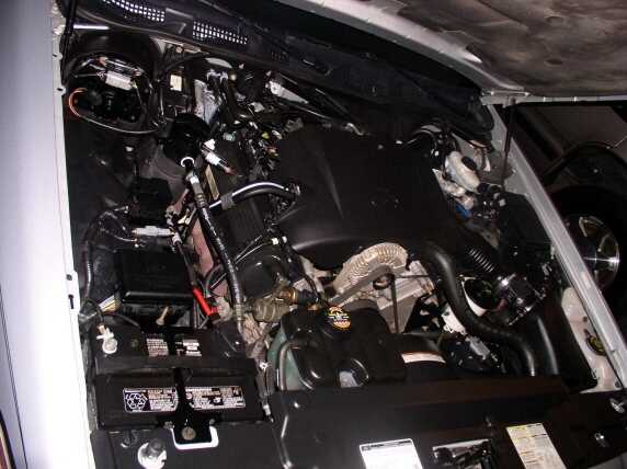 Engine bay of white sedan from passenger side showing V8 with black intake manifold and battery