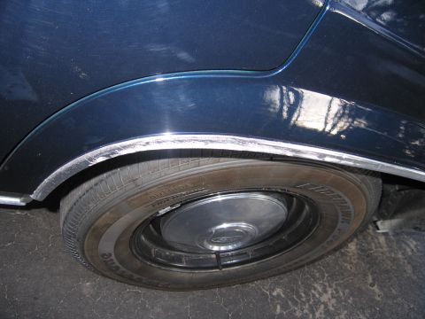 1991 Ford LTD Crown Victoria - Close-up view of the rear wheel well of a dark blue vehicle, showing the tire and chrome trim.