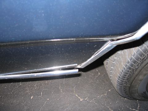 1991 Ford LTD Crown Victoria - Close-up of damaged chrome trim on a vehicle's lower body panel near the tire.