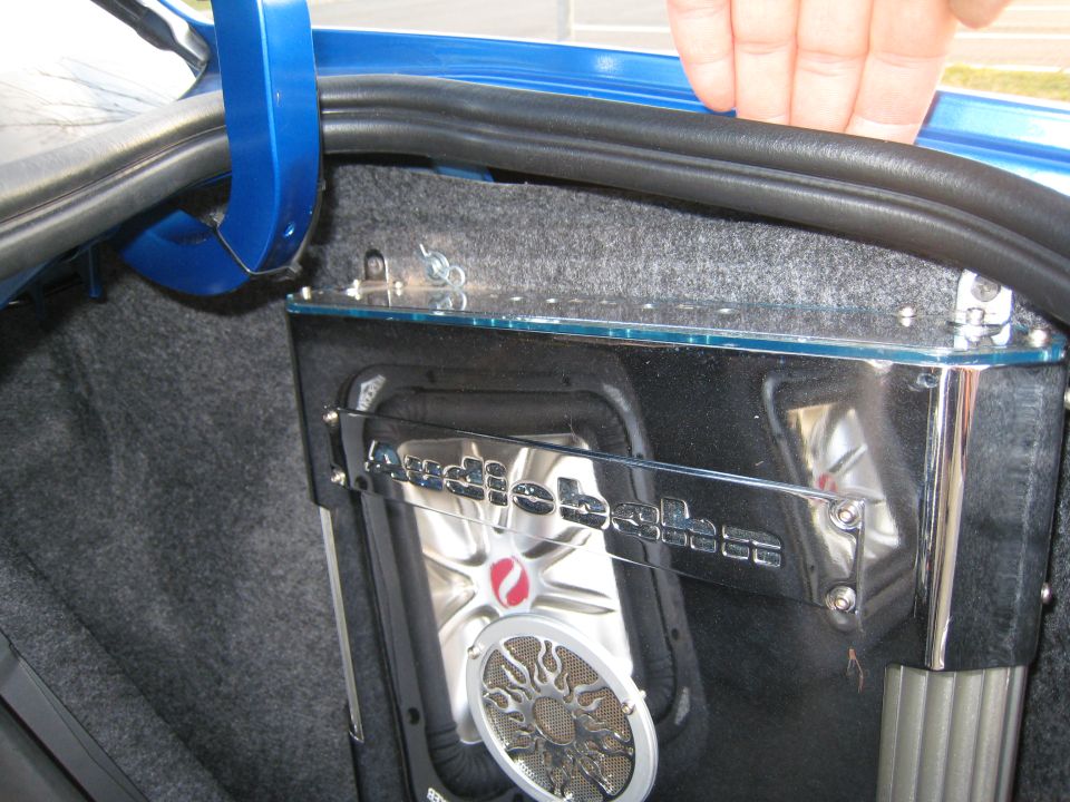 Car trunk with a subwoofer and chrome trim. A hand is visible near the trunk seal