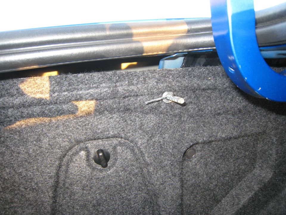 Gray carpeted trunk lining with a metal pin and clip. Blue painted metal trim is visible