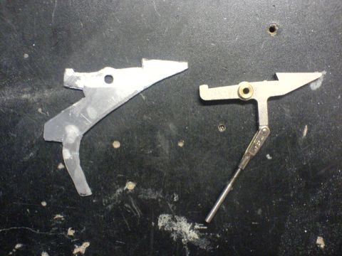 1985 Ford Bronco - Two metal linkage components are shown on a dark, textured surface.