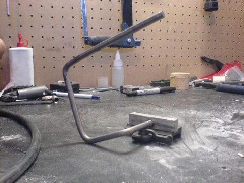 1985 Ford Bronco - A bent metal rod is secured to a workbench with a clamp, surrounded by tools and supplies.