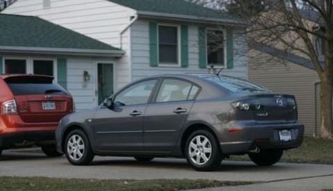 2008 Mazda 3 - A dark gray Mazda 3 sedan is parked in front of a house, with another vehicle to its left.
