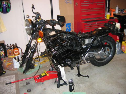 1985 Ford LTD Crown Victoria - A black motorcycle is disassembled in a garage, with tools and supplies nearby.