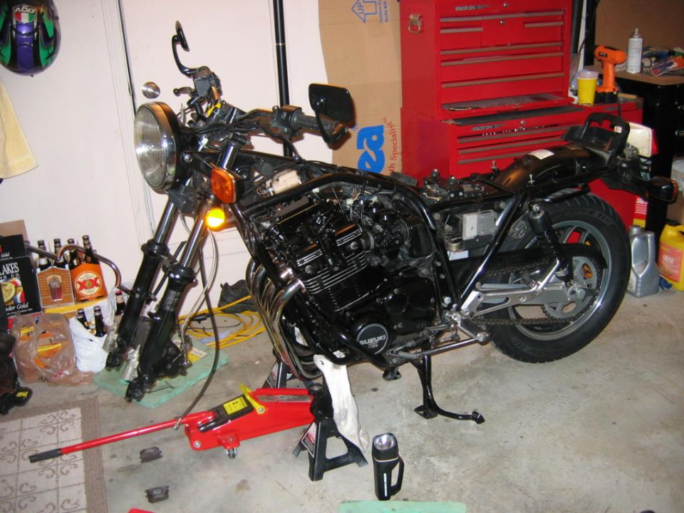Black motorcycle on stands with engine exposed, red toolbox in background