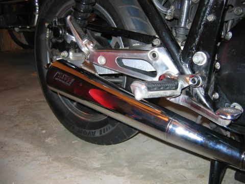 1985 Ford LTD Crown Victoria - Close-up view of a motorcycle's chrome exhaust pipe, showing the rear wheel and footpeg assembly.