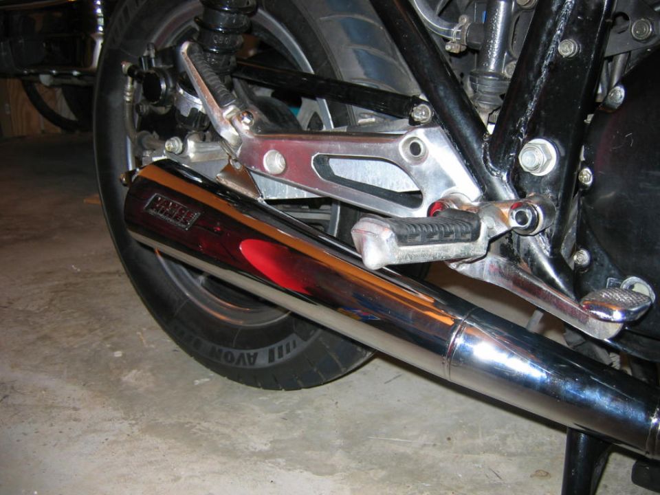 Chrome exhaust pipe with red reflection on motorcycle rear wheel and footpeg