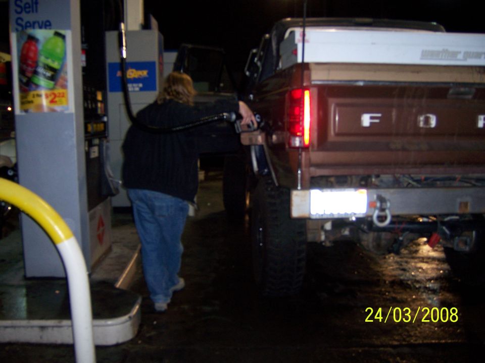 Person fueling a brown Ford F-Series truck at a gas station at night