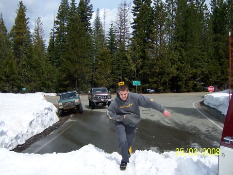 1991 Ford Bronco - A man runs through the snow past a 1991 Ford Bronco and another truck on a snowy road.