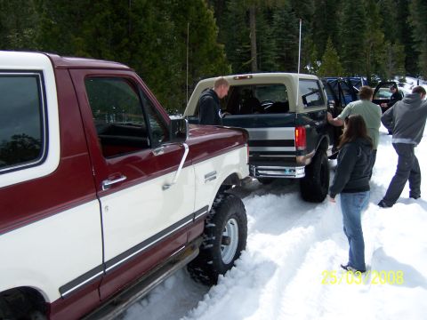 1991 Ford Bronco - Several people gather around two Ford Broncos parked in a snowy, wooded area.