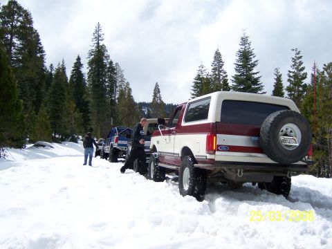1991 Ford Bronco - A line of off-road vehicles, including a red and white 1991 Ford Bronco, navigate a snow-covered trail.