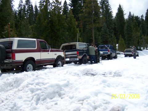 1991 Ford Bronco - Several off-road vehicles are stuck in the snow near a forest.