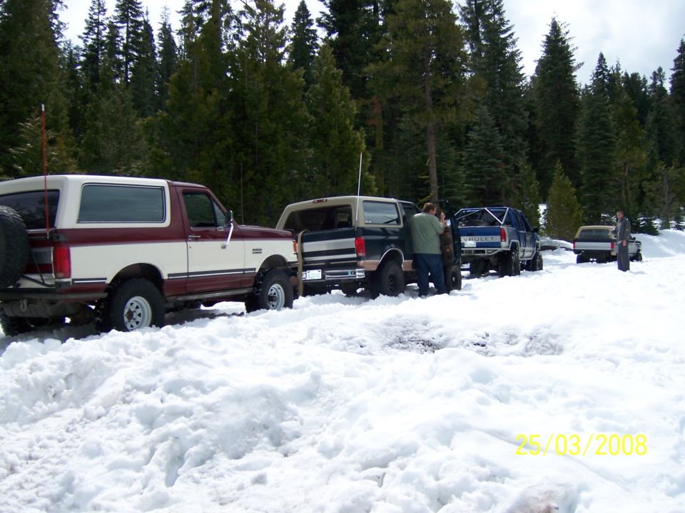 1991 Ford Bronco and other SUVs/trucks parked in deep snow with pine trees in background