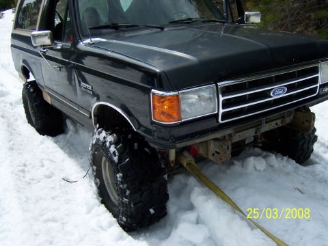 1991 Ford Bronco - A lifted black Ford Bronco is stuck in the snow with a tow strap attached to its front.