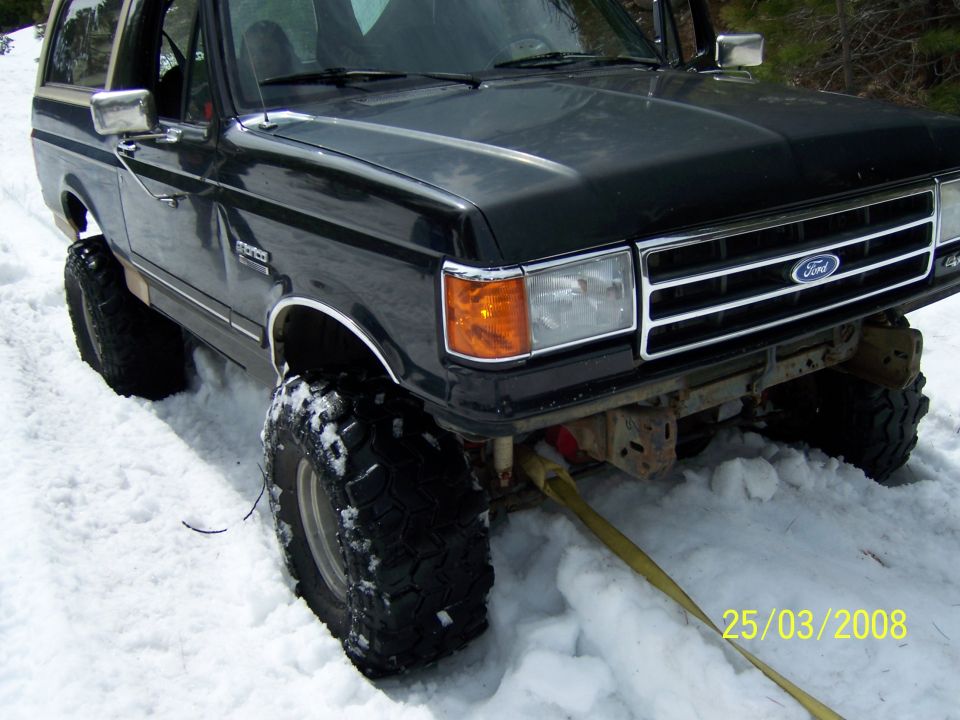 Black Ford Bronco with large tires stuck in snow, yellow tow strap attached to front bumper