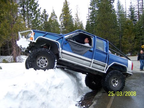 1991 Ford Bronco - A modified blue pickup truck navigates a snowy incline with a man inside.