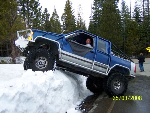 1991 Ford Bronco - A modified blue pickup truck navigates a snowbank on a wooded road, with a date stamp of 25/03/2008 visible.