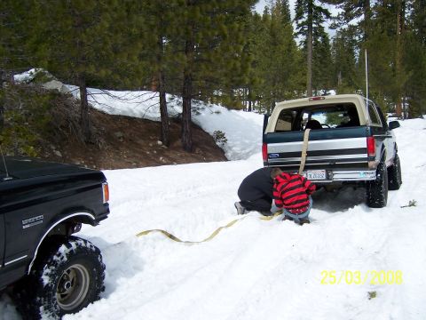 1991 Ford Bronco - Two people are working to free a Ford Bronco that is stuck in the snow, with another vehicle nearby.