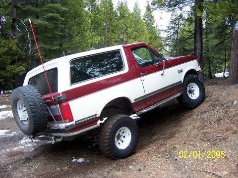 1991 Ford Bronco - A two-tone red and white Ford Bronco is seen off-road on a dirt trail with trees in the background.