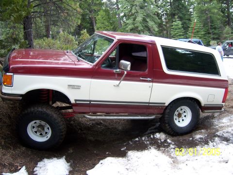 1991 Ford Bronco - Two-tone red and white 1991 Ford Bronco lifted for off-roading in a snowy wooded area.