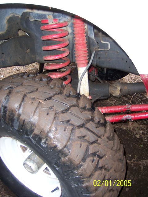 1991 Ford Bronco - Close-up of a vehicle's suspension system, including a tire covered in mud and red coil springs.