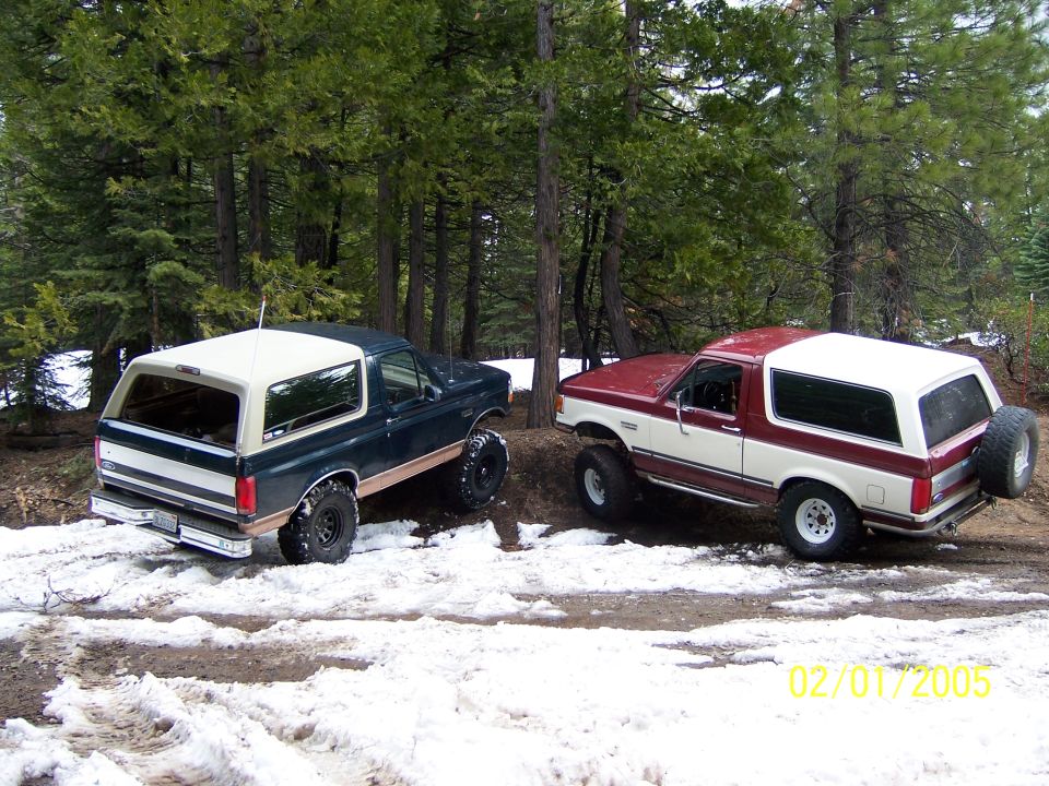 Two 1991 Ford Broncos in snow, one dark green and white, the other red and white