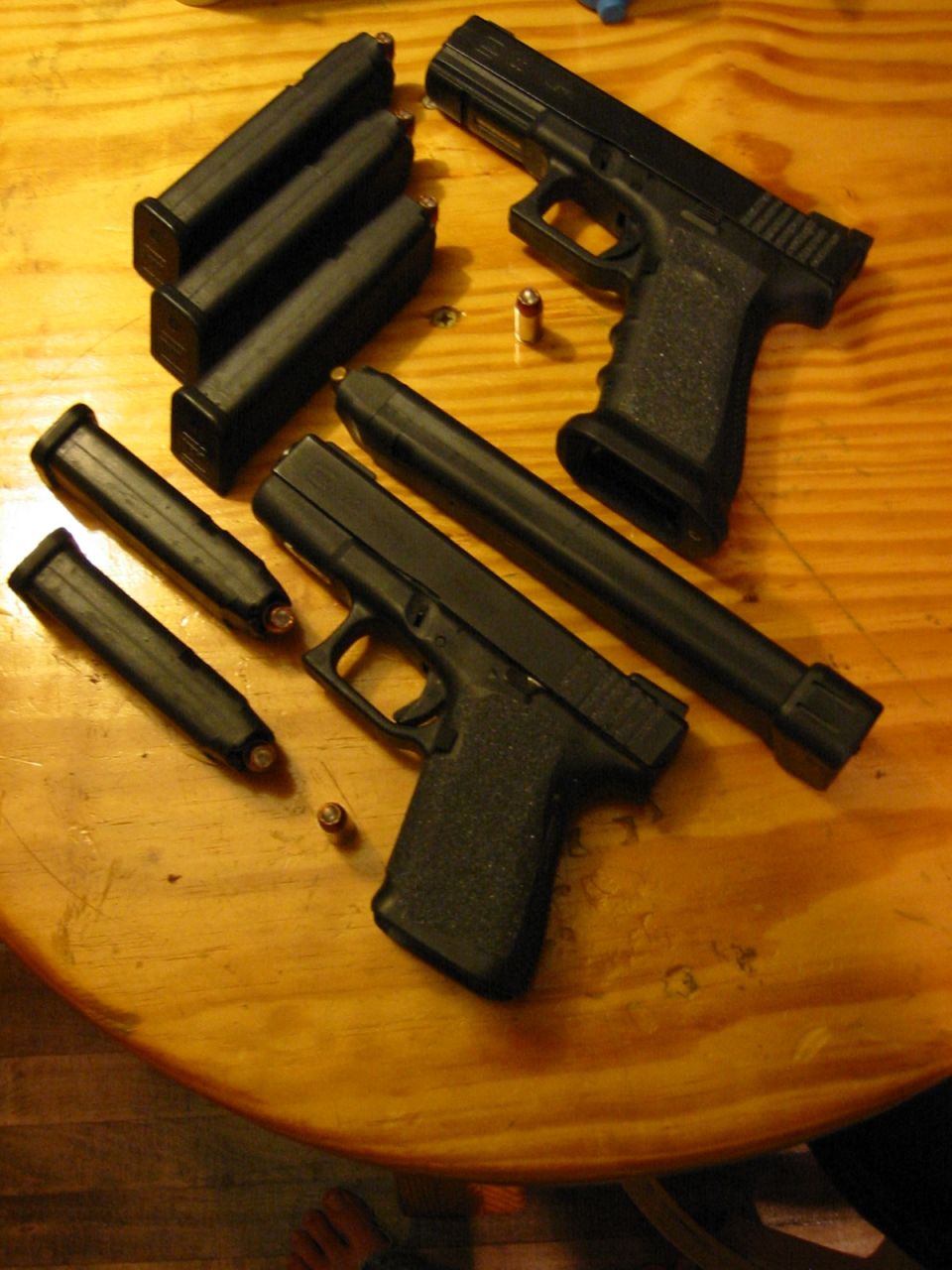 Two black handguns with several loaded magazines and loose cartridges on a wooden table