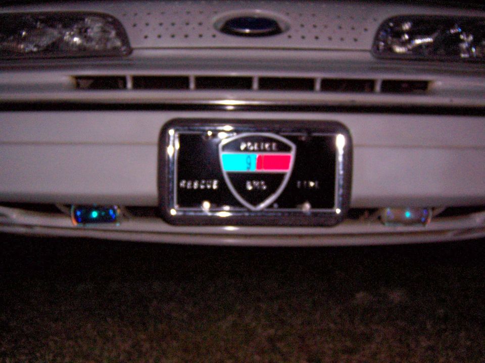 Front bumper of a white car with police/EMS plate and grille lights at night