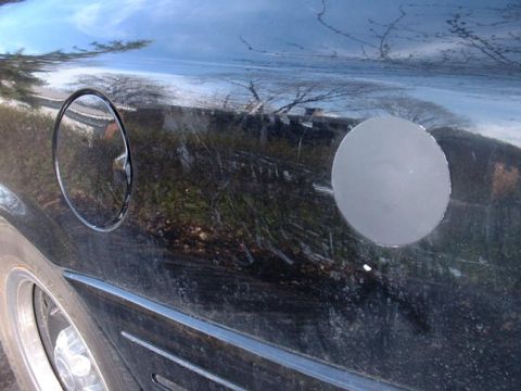 1998 Ford Crown Victoria - Side view of a car's body panel with a fuel door and a noticeable circular dent.