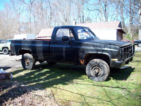 1987 Suzuki Samurai - A weathered black pickup truck sits in a grassy yard with a building and trees behind it.