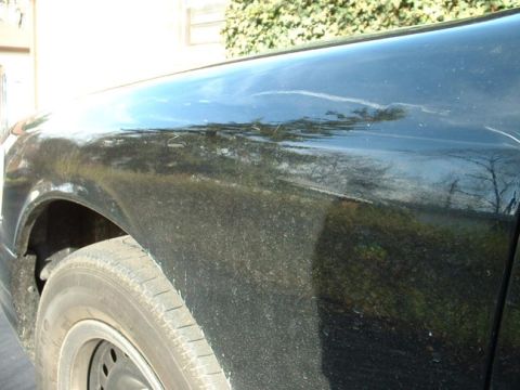 1998 Ford Crown Victoria - The side panel of a dark-colored vehicle shows reflections and some imperfections.