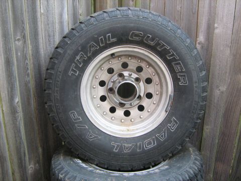 1993 Ford Bronco - A single tire and wheel assembly is shown, leaning against a weathered wooden fence.