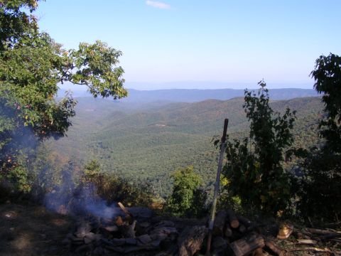1993 Ford Bronco - A scenic view of a forest valley with a campfire and stacked wood in the foreground.