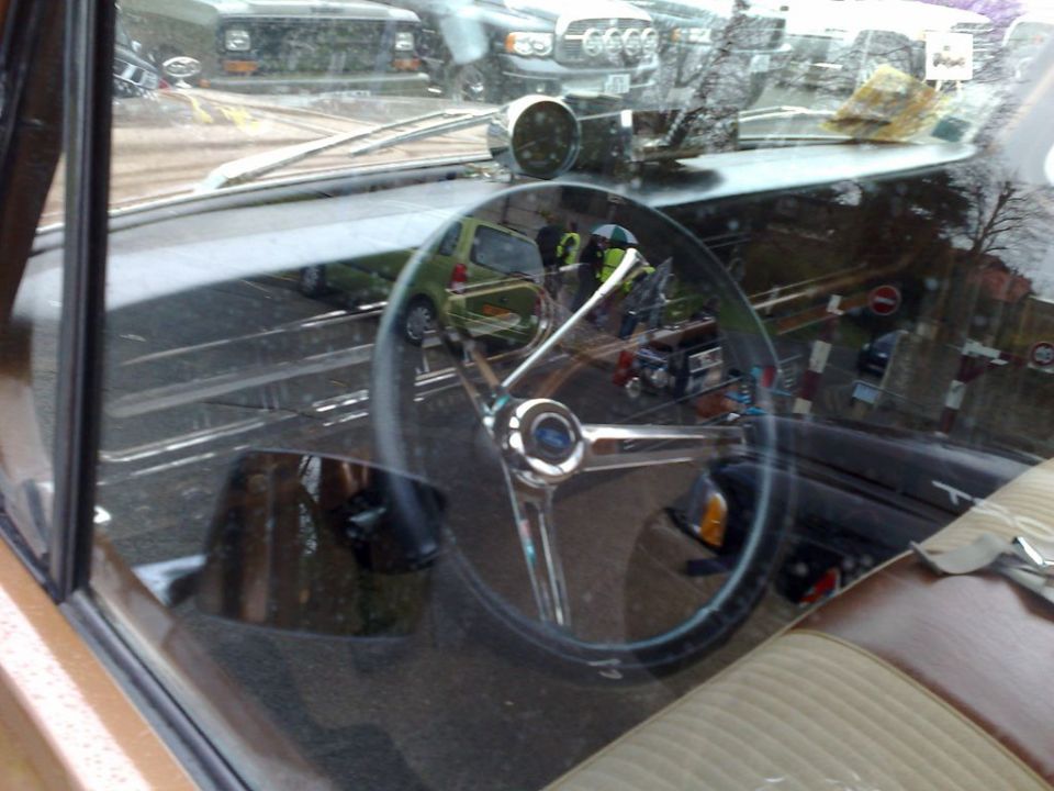 Interior shot of a car, showing the steering wheel and dashboard. Reflections in the windshield show other vehicles