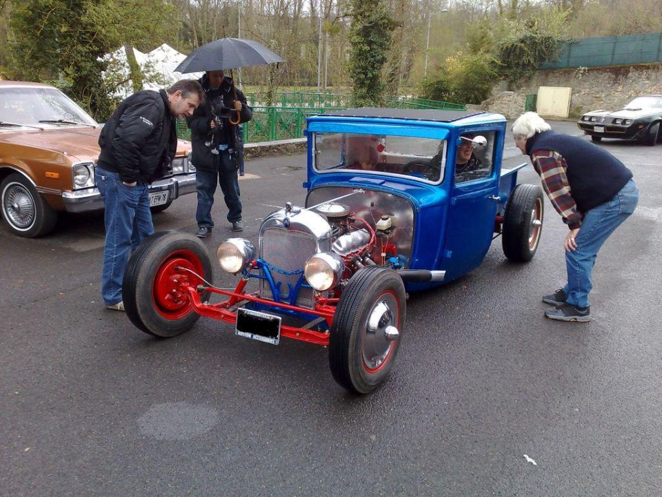 Blue hot rod pickup with exposed engine being admired at a show