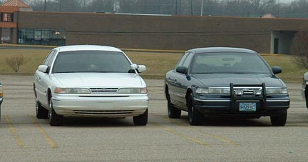 1998 Ford Crown Victoria - Two Ford Crown Victorias are parked side-by-side in a lot.