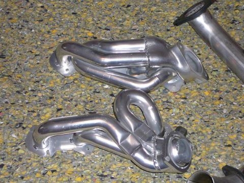 1997 Mercury Grand Marquis - Polished exhaust headers are shown laid out on a textured surface, with a section of exhaust pipe in the upper right corner.