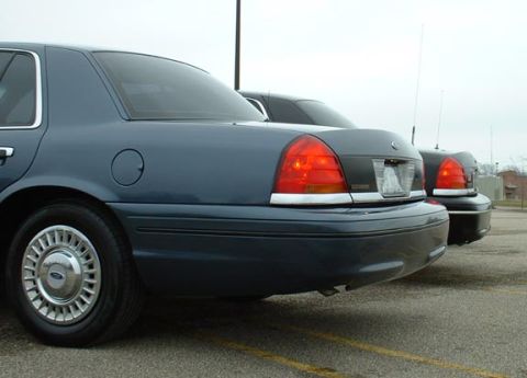 1998 Ford Crown Victoria - Two Ford Crown Victorias are parked side-by-side in a lot under an overcast sky.