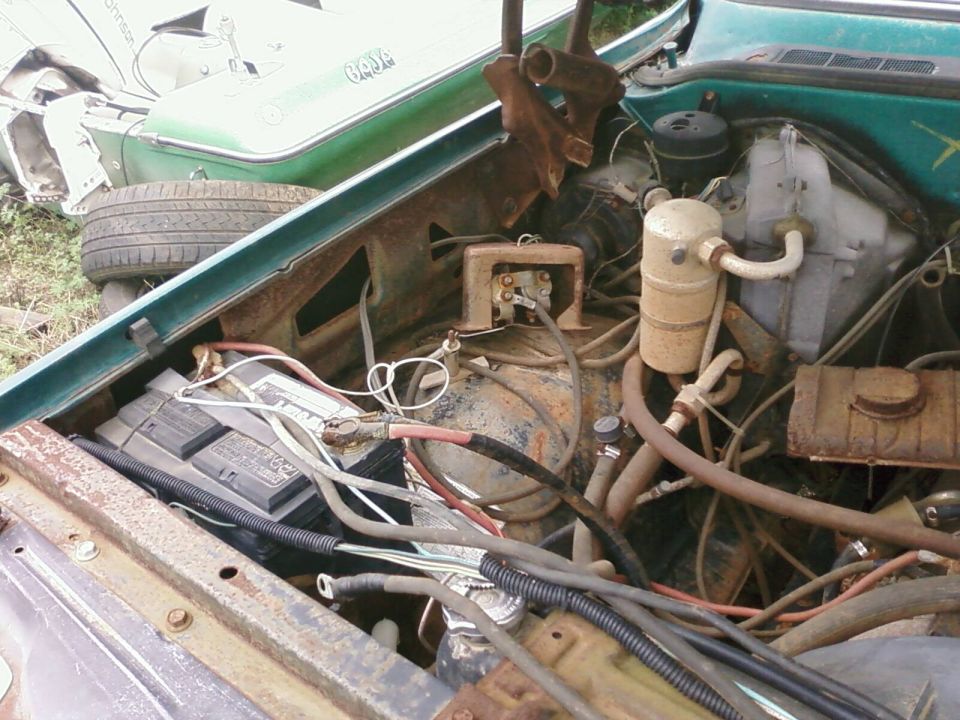 Rusty partly disassembled engine bay of green Chevrolet pickup with exposed wiring