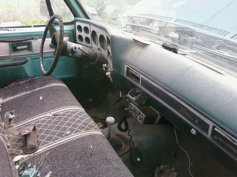Worn green Chevy square-body pickup interior with plaid bench seat, floor shifter and CB radio