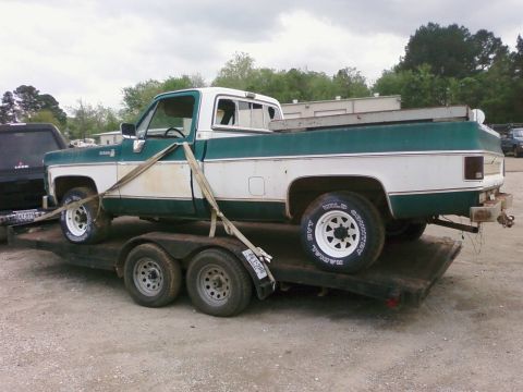 1979 Chevrolet Cheyenne - A two-tone pickup truck is being transported on a flatbed trailer under an overcast sky.