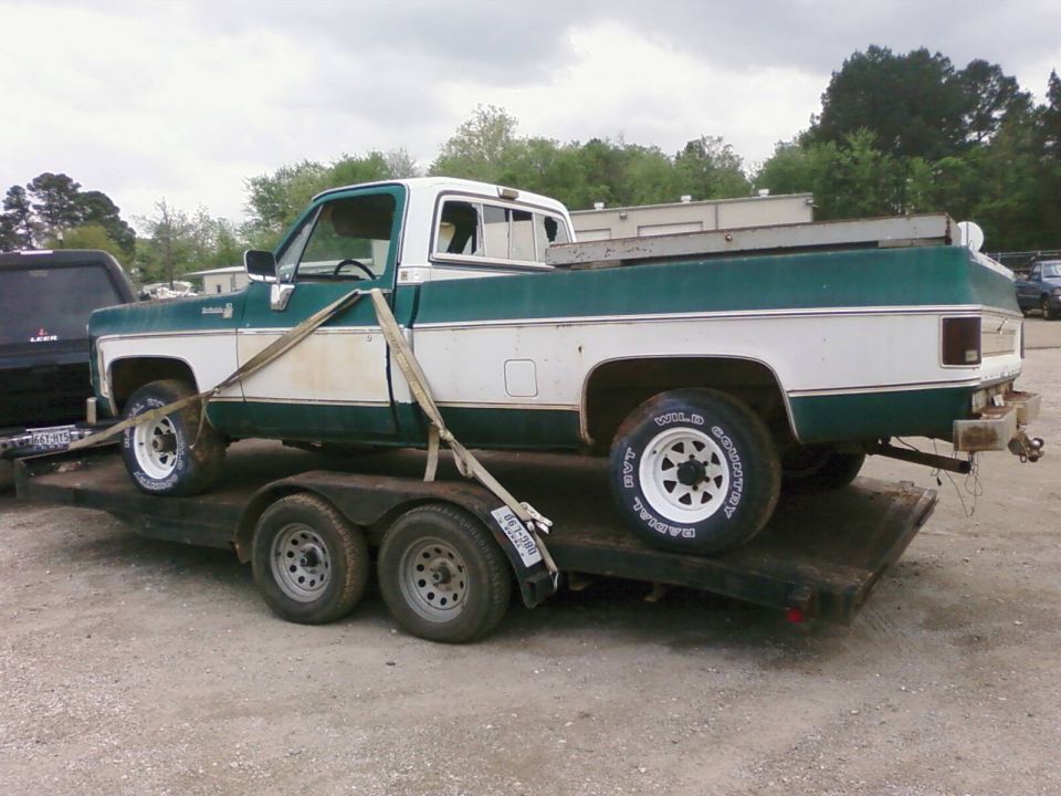 Green and white square-body Chevy pickup strapped on a flatbed trailer, side view