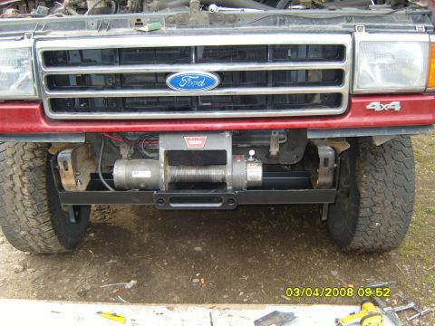 1989 Ford Bronco - Front view of a red Ford truck, likely a Bronco, a chrome grille, Ford emblem, and a Warn winch installed on a custom mount.