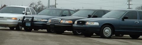 1998 Ford Crown Victoria - A line of four Ford Crown Victoria police cars are parked side-by-side.