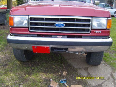 1989 Ford Bronco - Head-on view of a red late-1980s Ford truck front end with a blue Ford oval in the eggcrate grille, rectangular sealed-beam headlights with…