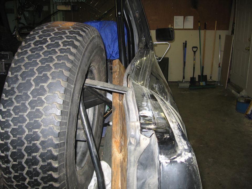 Spare tire mounted behind a damaged black vehicle door, propped open with wood