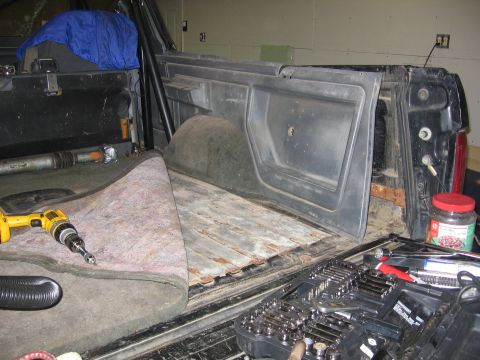 1989 Ford Bronco - Tools and a rolled-up carpet are visible in the cargo area of a vehicle with its rear door open.