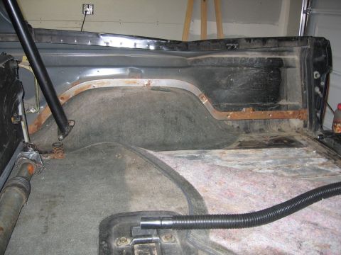 1989 Ford Bronco - The rear interior of a vehicle shows signs of wear and tear, with rust on the metal trim.