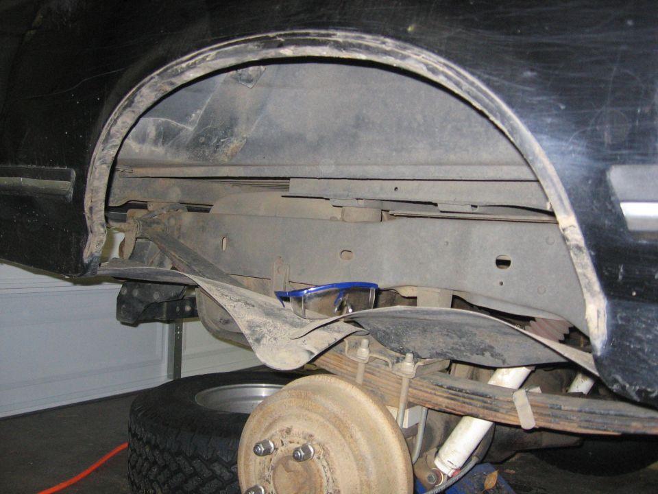 Black vehicle's rear wheel well and suspension with leaf springs, shocks, and brake drum visible